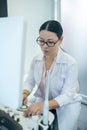 Female doctor in eyewear sitting at the ultrasonic device looking serious