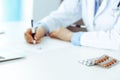 Female doctor filling up prescription form while sitting at the desk in hospital. Close-up of medical pills, lying at