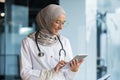 Female doctor in hijab works in modern clinic office, Muslim female doctor uses tablet computer, nurse in medical white Royalty Free Stock Photo