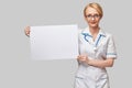 Female doctor holding a blank banner sign standing over grey background Royalty Free Stock Photo