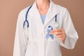 Female doctor holding blue ribbon on color background, closeup. Prostate cancer awareness concept Royalty Free Stock Photo