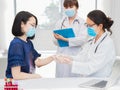 Female doctor holding woman hand in hospital, do medical checkup and staff is standing beside taking note on patient information Royalty Free Stock Photo