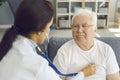 Female doctor listening to white-haired male patient`s heart through stethoscope