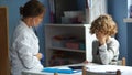 Female doctor listens to the lungs and bronchi in a teenager and writes the result on a medical record. Curly boy