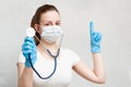 Female doctor in mask with a stethoscope shows a finger to the side