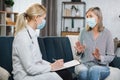 Female doctor or nurse listening to sick senior woman patient and writing prescription during home visit. Doctor and Royalty Free Stock Photo