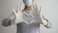 Female doctor or nurse with a medical mask and hands in latex white gloves shows the symbol of the heart. Negative space. Royalty Free Stock Photo