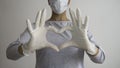 Female doctor or nurse with a medical mask and hands in latex white gloves shows the symbol of the heart. Negative space. Royalty Free Stock Photo