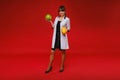 A female doctor nurse in a white coat with fruit in her hands poses on a red background, melon, watermelon