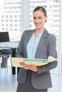 Female professional standing in modern office holding papers in manila folder near desk and windows Royalty Free Stock Photo