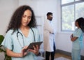 Female doctor in scrubs uses digital tablet with medical team in background Royalty Free Stock Photo