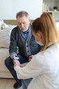 Female doctor senior man taking his blood pressure in doctor office or at home. Old man patient and doctor have Royalty Free Stock Photo