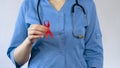 Female doctor showing red ribbon, AIDS awareness symbol, venereal disease risk