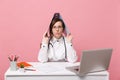 Female doctor sit at desk work on computer with medical document hold folder in hospital isolated on pastel pink wall Royalty Free Stock Photo