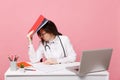 Female doctor sit at desk work on computer with medical document hold folder in hospital isolated on pastel pink wall Royalty Free Stock Photo