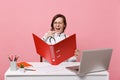 Female doctor sit at desk work on computer with medical document hold folder in hospital isolated on pastel pink wall Royalty Free Stock Photo