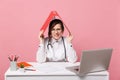 Female doctor sit at desk work on computer with medical document hold folder in hospital isolated on pastel pink wall Royalty Free Stock Photo