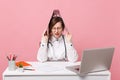 Female doctor sit at desk work on computer with medical document hold folder in hospital isolated on pastel pink wall Royalty Free Stock Photo