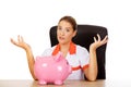 Female doctor sitting behind the desk and holding a piggybank