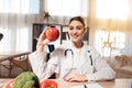 Female doctor sitting at desk in office with microscope and stethoscope. Woman is holding red apple. Royalty Free Stock Photo