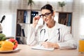 Female doctor sitting at desk in office with microscope and stethoscope. Woman is writing on clipboard. Royalty Free Stock Photo
