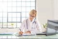 Female doctor sitting at desk and using laptop and doing some paperwork in doctorÃ¢â¬â¢s office