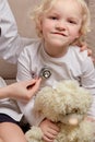 A female doctor sitting on a sofa listens to a child heart with a phonendoscope.