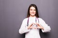Female doctor smile and make her hand to heart shape on grey