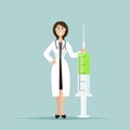 The female doctor smiles and stands next to a large syringe. A syringe with a vaccine.