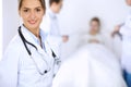 Female doctor smiling on the background with patient in the bed and two doctors Royalty Free Stock Photo