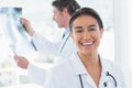 Female doctor smiling at camera while her colleague looking at X-ray Royalty Free Stock Photo