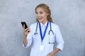 Female doctor smiling and looking in smartphone isolated over grey background