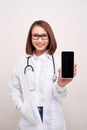 Female doctor smiling and showing a blank smart phone screen isolated on a white background Royalty Free Stock Photo