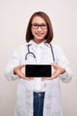 Female doctor smiling and showing a blank smart phone screen isolated on a white background Royalty Free Stock Photo