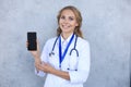 Female doctor smiling and showing a blank smartphone screen isolated over grey background Royalty Free Stock Photo