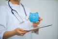 Female Doctor with Stethoscope Holding Piggy Bank and tablet computer. Perfect medical service in clinic. Modern Royalty Free Stock Photo