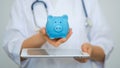 Female Doctor with Stethoscope Holding Piggy Bank and tablet computer. Perfect medical service in clinic. Modern Royalty Free Stock Photo