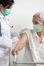 Female doctor with syringe doing injection vaccine COVID-19 in the shoulder or arm of senior woman,asian nurse injecting,