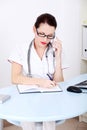 Female doctor talking by the phone and writing. Royalty Free Stock Photo