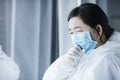 Female doctor tired and cough in protective suit before windows