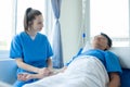 Female doctor treating young male patient in bed and talking with Asian male patient beside bed Royalty Free Stock Photo