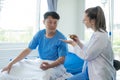 Female doctor treating young male patient in bed and talking with Asian male patient beside bed Royalty Free Stock Photo