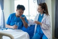 Female doctor treating young male patient in bed and talking with Asian male patient beside bed Royalty Free Stock Photo