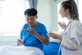 Female doctor treating young male patient in bed and talking with Asian male patient beside bed Royalty Free Stock Photo