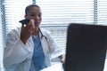 Female doctor using laptop while talking on mobile phone at desk Royalty Free Stock Photo