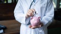 Female doctor is using stethoscope to piggy bank, saving protection concept Royalty Free Stock Photo