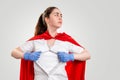 A female doctor, wearing medical gloves and a red superhero Cape, tears her coat on her chest. Gray background. The concept of the