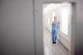 Female Doctor Wearing Scrubs In Hospital Corridor Using Digital Tablet Viewed Through Window In Door Royalty Free Stock Photo