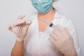 Female doctor in a white coat, medical cap, mask and gloves works with a syringe needle and a medical ampoule. A scientist in ster