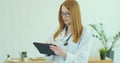 Female doctor in white coat using modern TabletPC device with touch screen. Doctor using DigitalTablet texting to